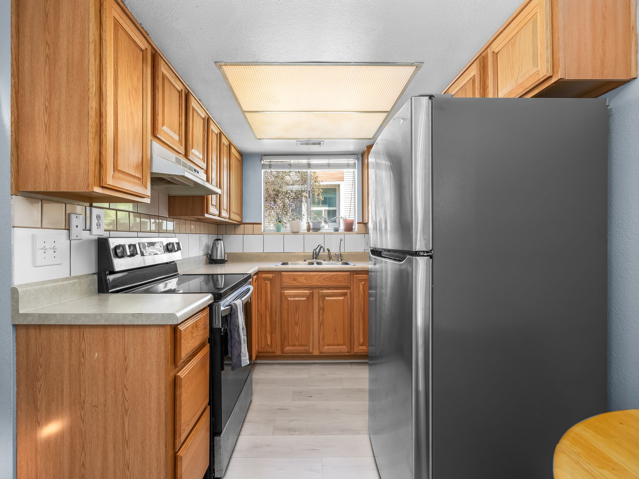 Kitchen featuring light wood cabinetry, light countertops, white tiled backsplash, stainless steel refrigerator, and wood-finish flooring