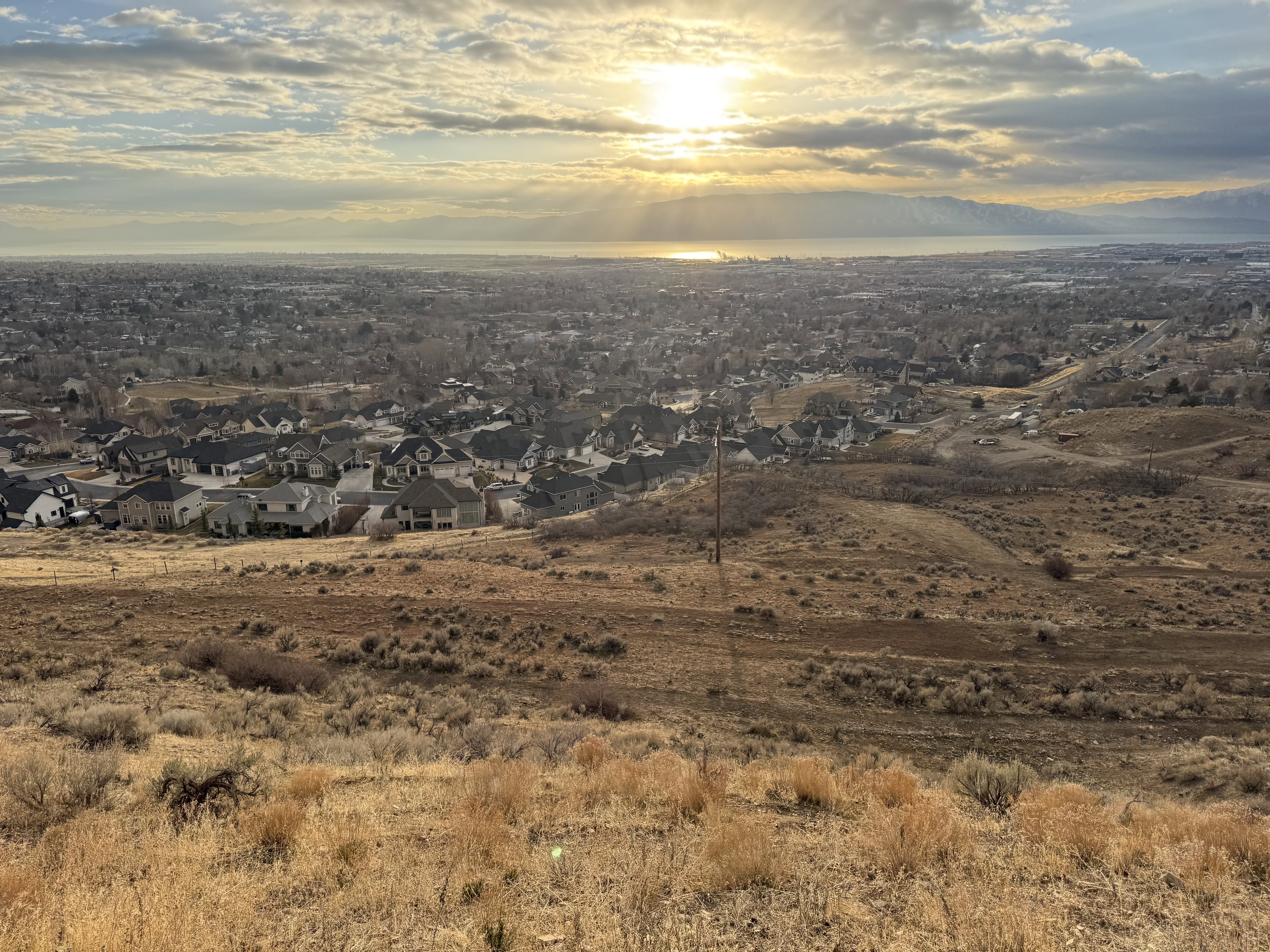 Expansive residential landscape featuring a distant body of water, mountains, and a clear sky with visible sunlight