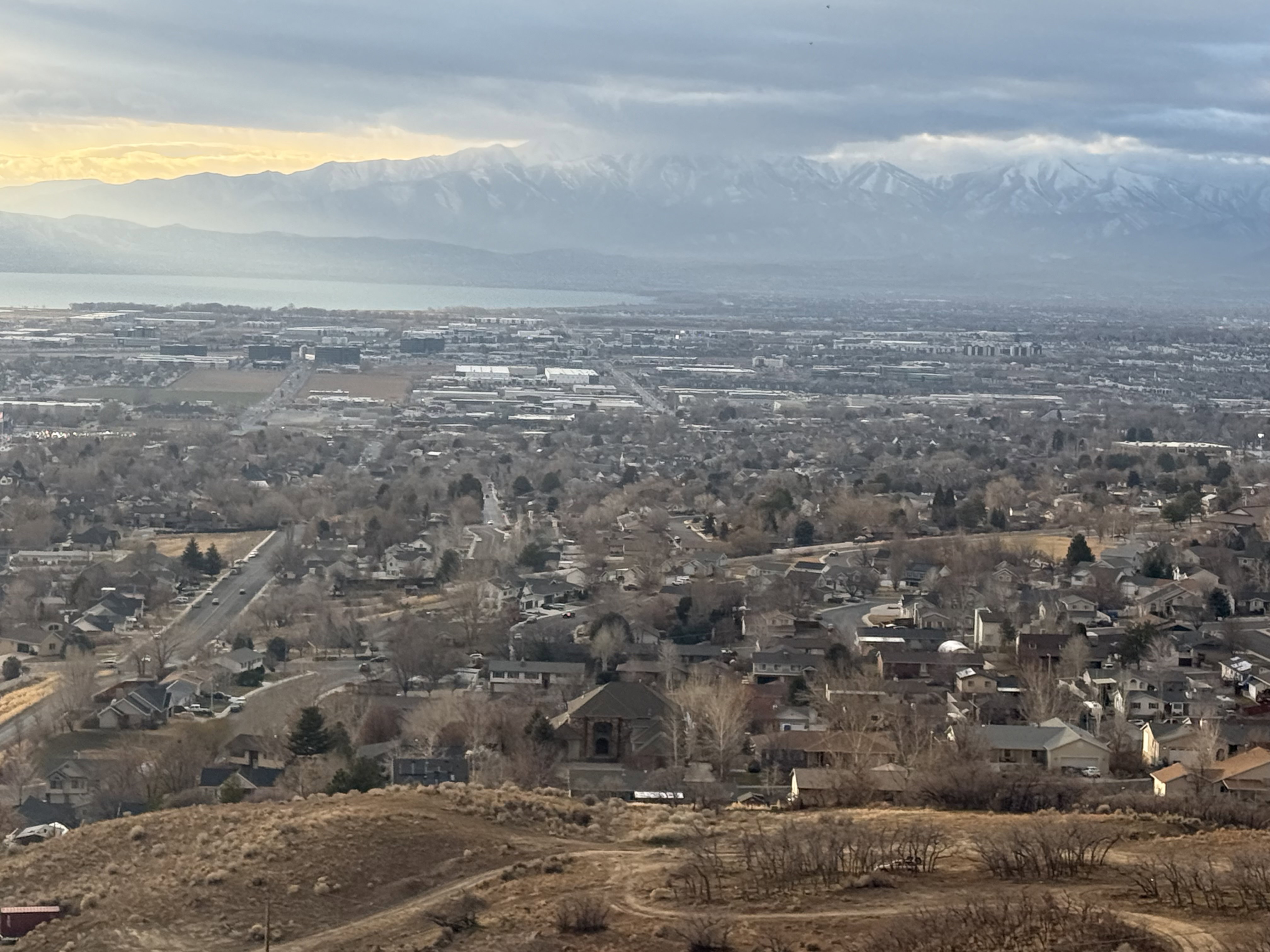 Expansive regional panorama featuring distant snow-capped mountains, a large body of water, and a widespread residential landscape