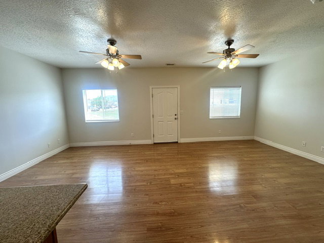 Spacious room featuring wood-finish flooring, two ceiling fans with integrated lighting, and neutral wall tones