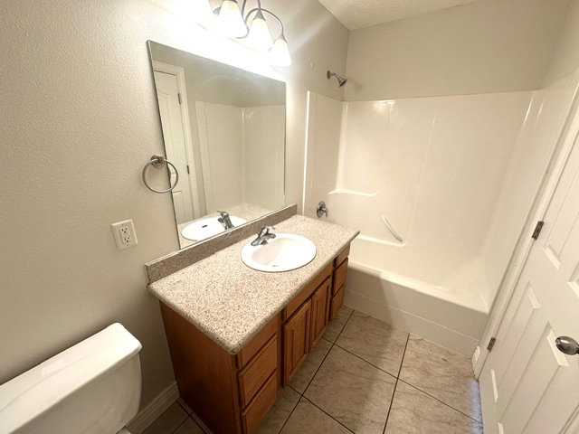 Bathroom featuring a single vanity with a laminate countertop, light wood-finish cabinetry, a mirror, and a three-light fixture