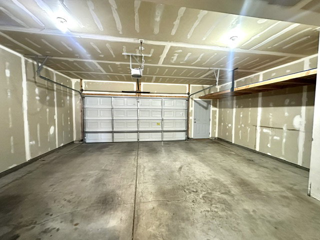 Spacious garage featuring a paneled overhead door, concrete flooring, overhead lighting, and built-in shelving