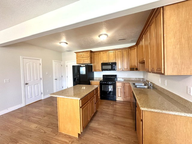 Kitchen featuring wood-finish flooring, a central island, granite countertops, wood cabinetry, and black appliances