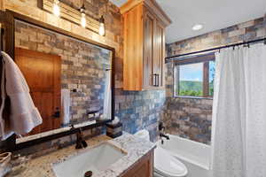 Bathroom featuring a textured brick-style wall, a white undermount sink, a stone-finish countertop, and a wood-finish vanity cabinet