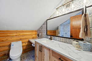 Bathroom featuring an angled white ceiling and log wall paneling