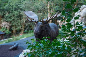 Sculpted moose figure within a landscaped setting featuring rock formations and mature foliage