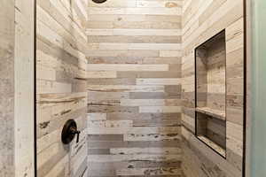 Shower enclosure featuring plank-style porcelain tile walls, a built-in niche with a solid surface shelf, a rain showerhead, and a bronze-finish control valve