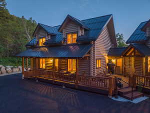 Log cabin exterior featuring a dark metal roof, multiple dormer windows, and a wraparound porch with wood railings