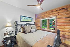 Bedroom featuring a log wall, a wood-framed window, and a ceiling fan with integrated lighting