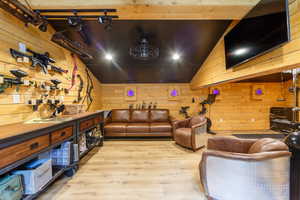Finished room featuring wood-finish flooring, plank wood wall finishes, a dark sloped ceiling, recessed lighting, and a wall-mounted television