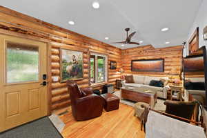 Living room featuring natural wood log walls, light wood-finish flooring, and recessed ceiling lighting