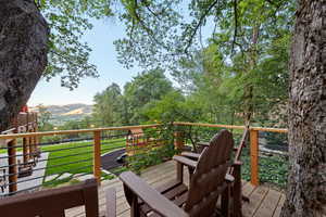 Wood-plank deck with Adirondack chairs, featuring a cable railing system, overlooking a manicured lawn with distant mountains