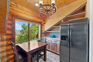 Kitchen space featuring natural wood log walls and ceiling, stainless steel refrigerator, built-in shelving, and light-toned countertops