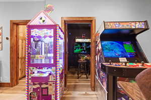Gaming room featuring a vibrant purple crane game, a classic arcade cabinet, and wood-finish flooring