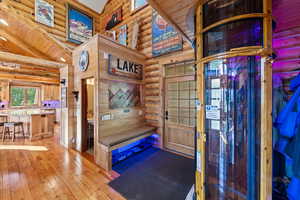 Architectural wood-framed elevator with clear paneling, hardwood flooring, wood-paneled walls, a built-in bench with cushion, and a wood-panel entry door
