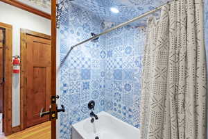 Bathroom featuring a shower-over-tub combination with blue patterned wall and ceiling tiling, black fixtures, and a white tub