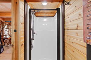 Compact shower stall with a white surround and dark bronze fixtures, framed by natural wood plank walls and a wood-finish ceiling