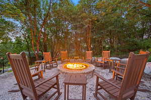 Outdoor fire pit area featuring a stone-clad fire pit, surrounding gravel ground cover, and natural wood rocking chairs