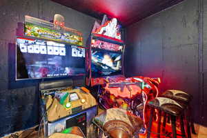 Dedicated entertainment space featuring arcade machines with integrated screens, accompanying stools, and dark-finished walls