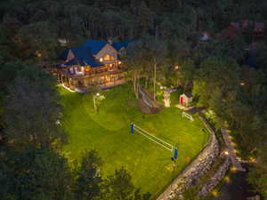 Custom-built residence featuring a spacious wood deck, expansive lawn with sports court, and an adjacent wooded hillside
