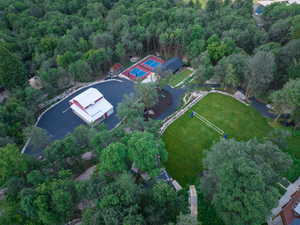Expansive property featuring a red and white barn structure, multiple paved driveways, a vibrant green lawn with volleyball net, and a dedicated sports court with blue and red surfacing