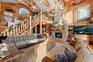 Spacious living area featuring a stone fireplace, log walls and ceiling beams, a spiral log staircase, and an arched window