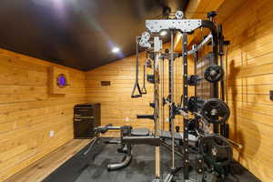 Dedicated fitness space featuring wood-paneled walls, sloped ceiling with recessed lighting, and rubber mat flooring