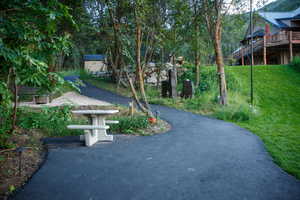 Paved path with a stone picnic table, surrounded by mature trees and verdant landscaping