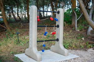 Outdoor recreation area featuring a permanent "Ladder Toss" game structure with red and blue bolas, set on a concrete pad amidst natural landscaping