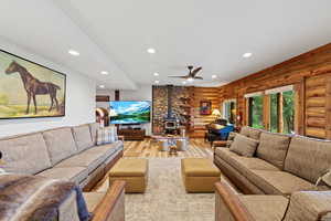 Spacious living area featuring log wall construction, wood-finish flooring, recessed lighting, a stone-faced fireplace with a wood-burning stove, and a ceiling fan