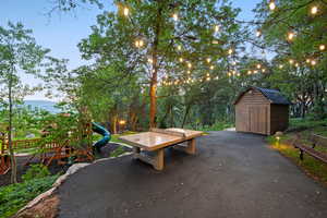 Paved path with string lighting, a solid surface outdoor table, and a wooden storage shed