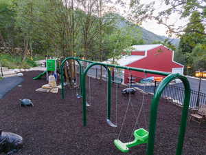 Outdoor play area featuring a swing set with two swings, a slide structure, and protective ground covering