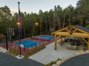Outdoor entertainment area featuring a wooden gazebo with a shingled roof, concrete patio, multi-sport court, and mature trees