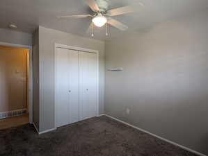 Bedroom featuring neutral gray walls, dark gray carpeting, and a white ceiling fan with integrated lighting