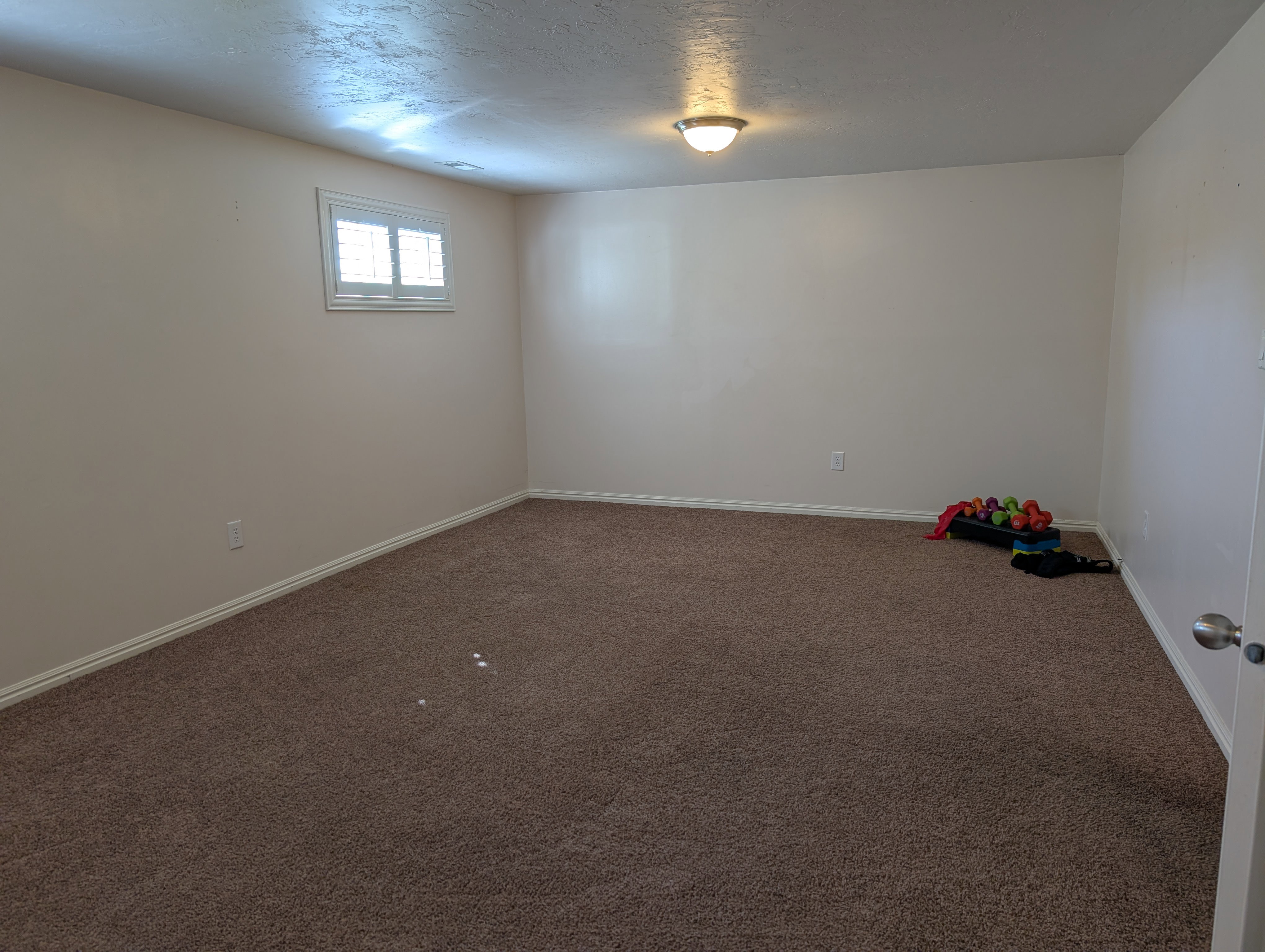 Spacious multipurose room featuring neutral carpeting, light-toned walls, and a single window with plantation-style shutters