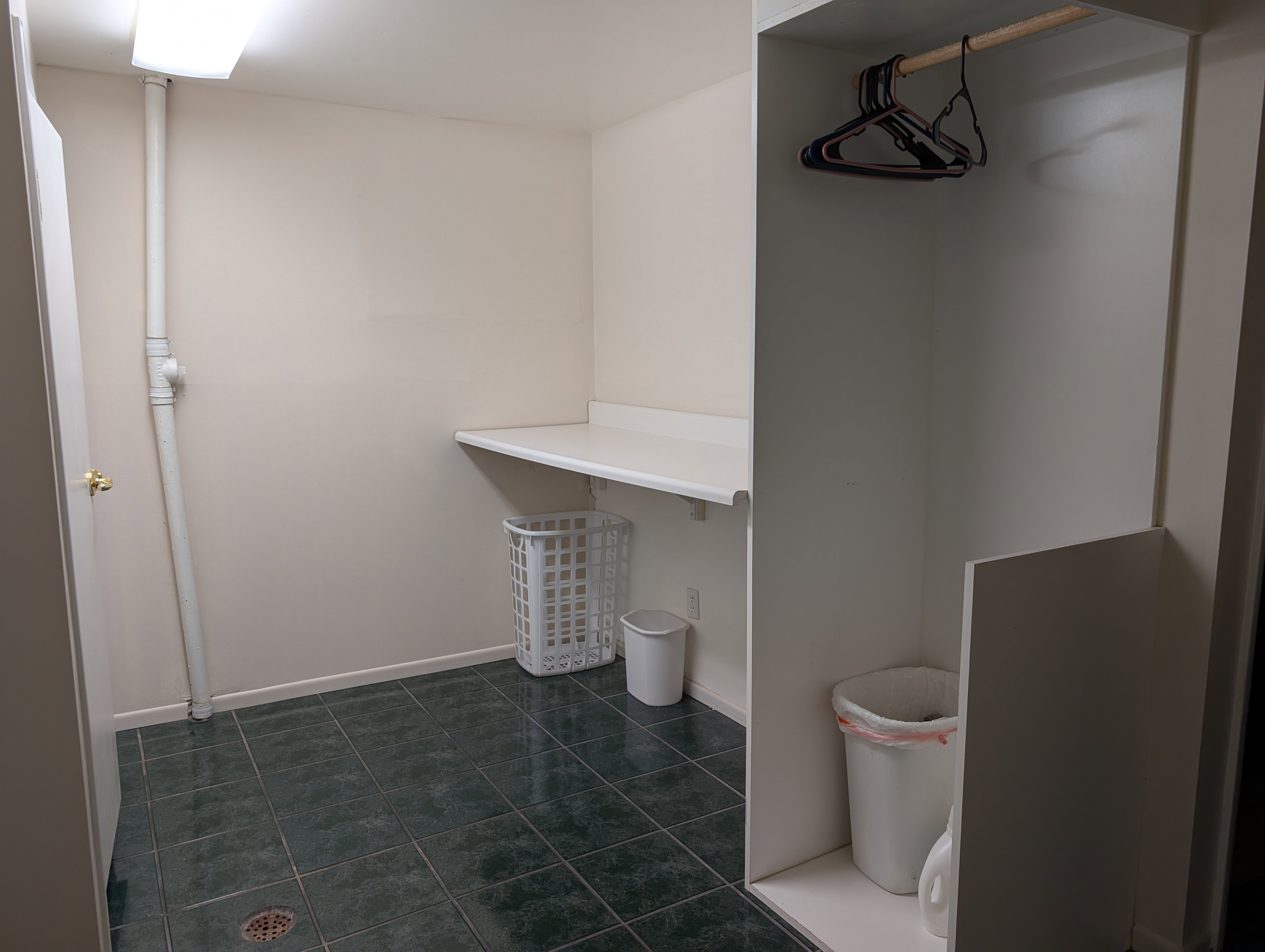 Laundry area featuring dark green square floor tiles, a built-in white countertop, and a clothes hanging rod within an alcove