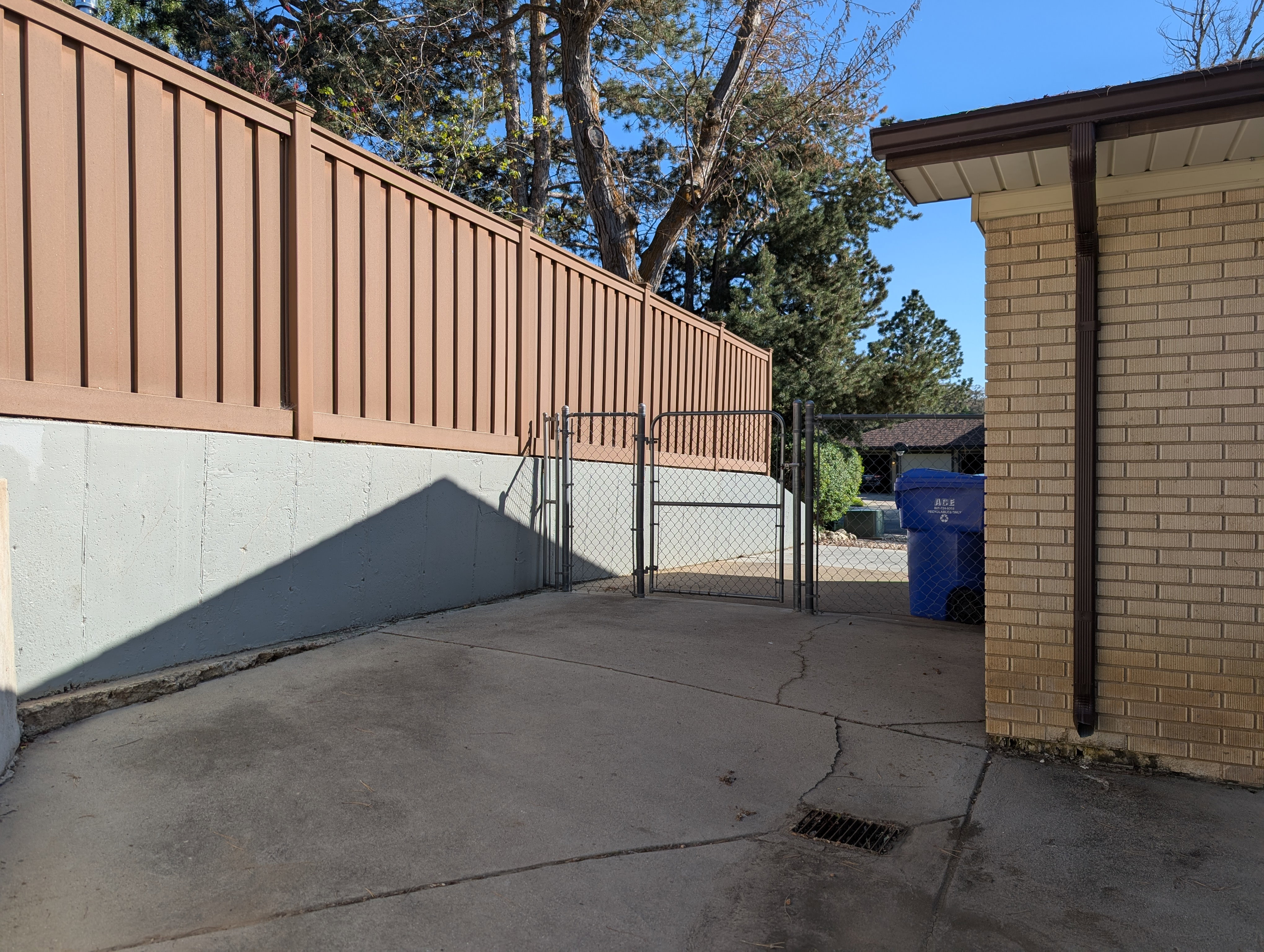 Paved concrete surface bordered by a light brown privacy fence atop a concrete retaining wall