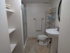 Bathroom featuring a pedestal sink with a brushed nickel faucet, a toilet, and a shower with a sliding glass door
