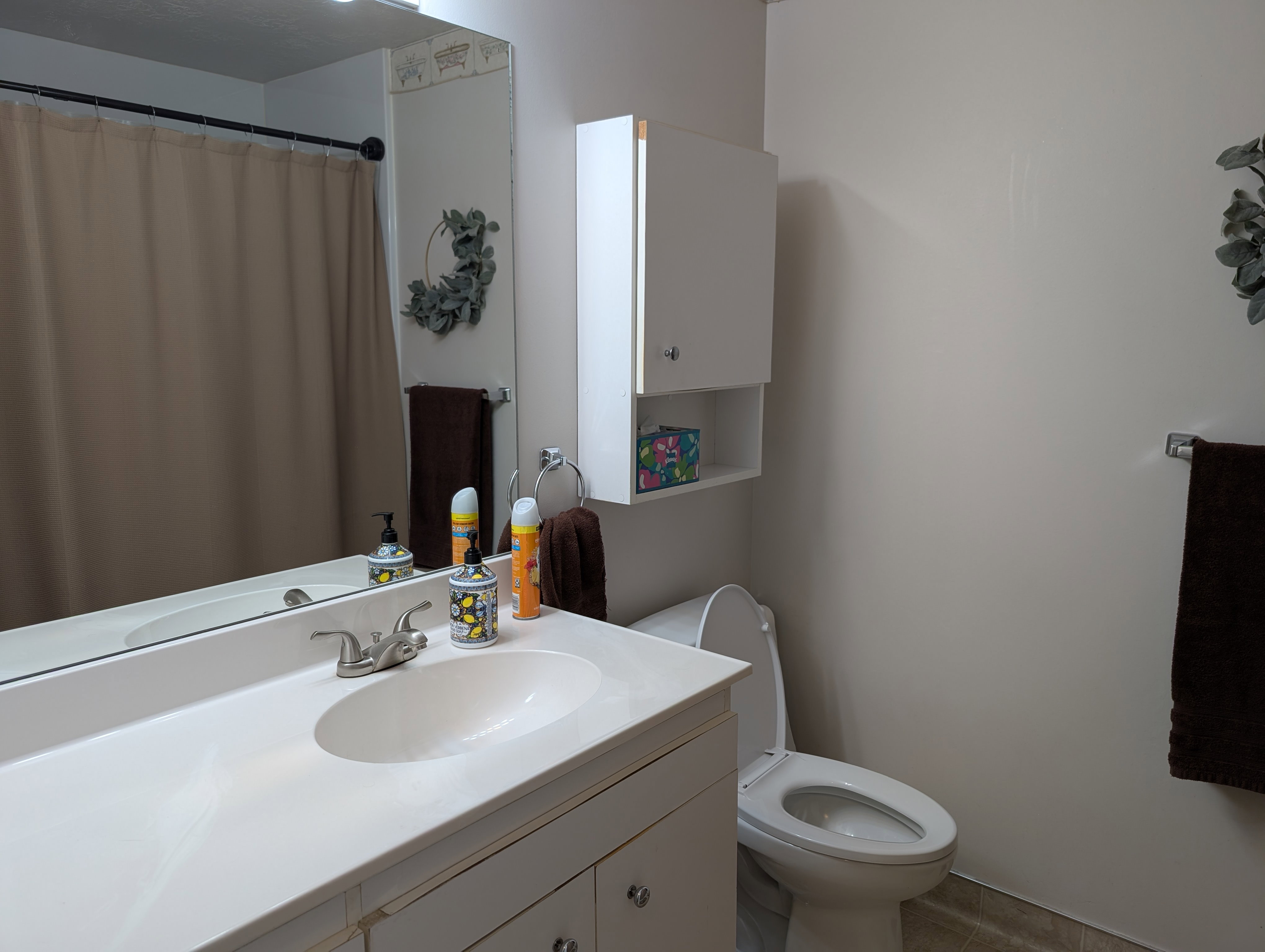 Bathroom vanity with integrated sink and chrome faucet, large wall mirror, and overhead cabinet storage