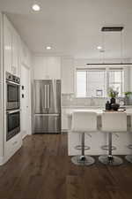Kitchen featuring stainless steel appliances, white cabinetry, a kitchen breakfast bar, dark wood finished floors, and recessed lighting