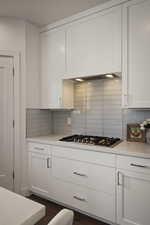 Kitchen featuring white cabinets, dark wood-style flooring, stainless steel gas stovetop, a textured ceiling, and light stone counters