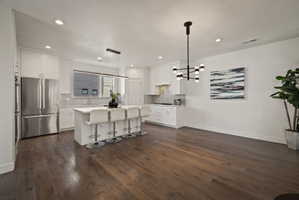 Kitchen featuring a breakfast bar, a center island, stainless steel appliances, white cabinets, and dark wood-style flooring