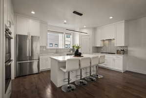 Kitchen with stainless steel appliances, a breakfast bar, white cabinetry, dark wood-style floors, and a textured ceiling