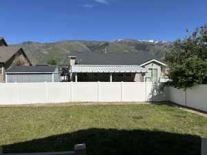 Expansive backyard featuring a manicured lawn, white privacy fencing, and a mountain backdrop with snow-capped peaks