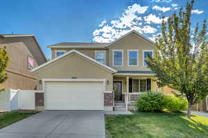 Stucco exterior featuring a two-car garage, brick accents, and a covered porch