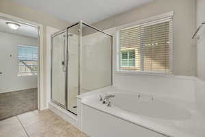 Bathroom featuring a built-in soaking tub with chrome fixtures, a glass-enclosed shower, a window with horizontal blinds, and tiled flooring