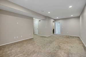 Spacious room featuring neutral carpeting, light gray wall paint, white trim, recessed ceiling lighting, and multiple doorways