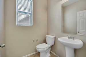 Powder room featuring a pedestal sink with a chrome faucet, a rectangular wall mirror, and a window with horizontal blinds