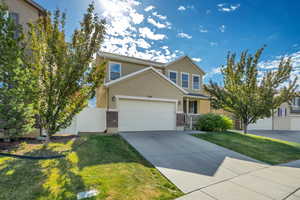 Two-story stucco and brick facade residence featuring a two-car garage, mature trees, a well-maintained lawn, and a paved driveway