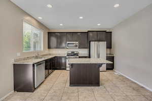 Kitchen featuring dark wood cabinetry, light-toned granite countertops, and stainless steel appliances
